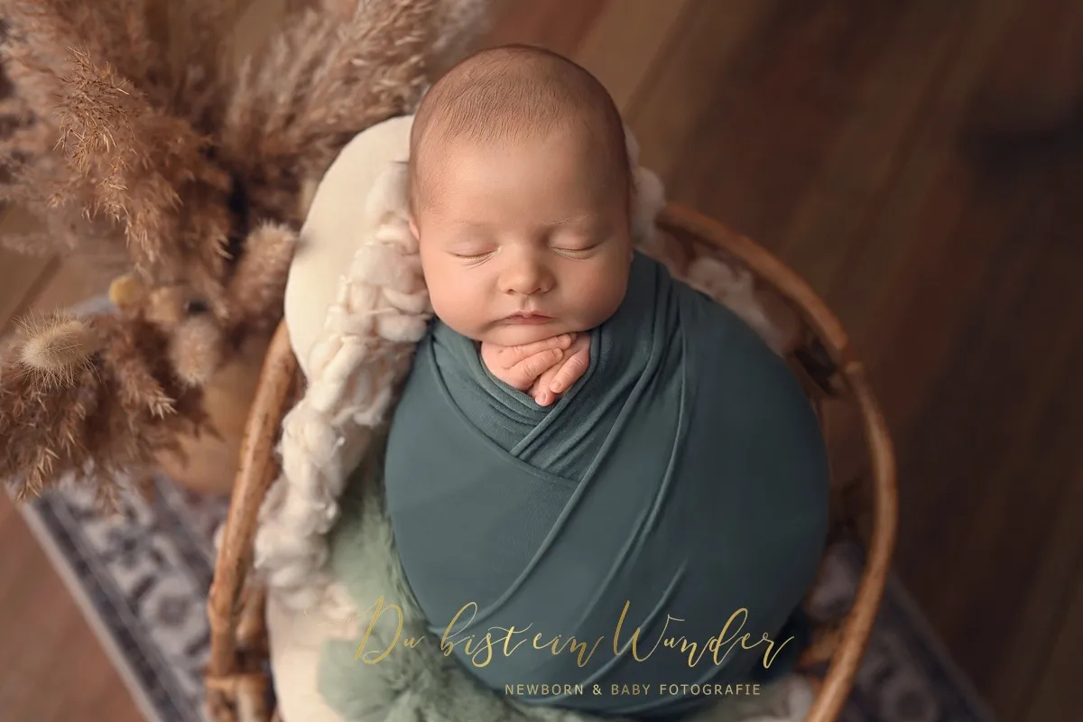 Schlafendes Baby in grünem Wrap im Weidenkorb dekoriert mit Pampasgras