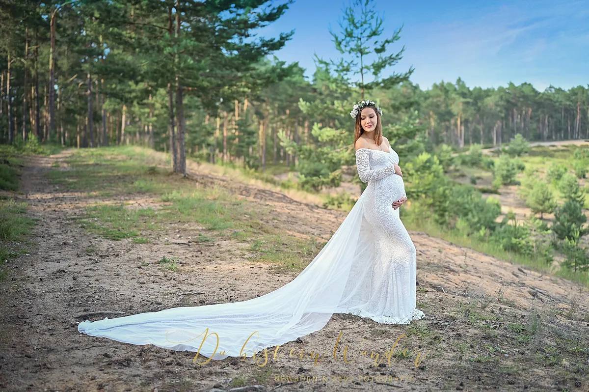 Schwangere in weißem Spitzenkleid mit Blumenkranz in der Heide