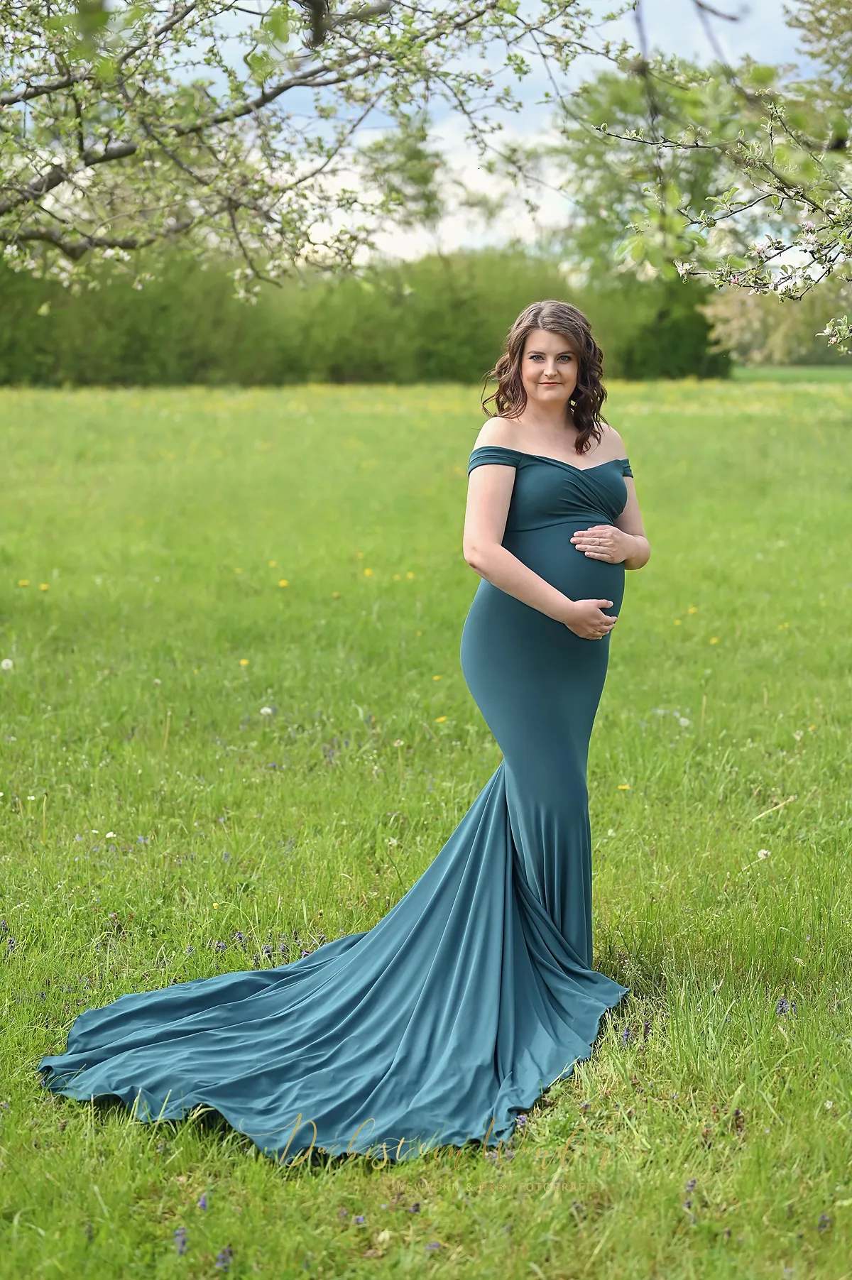 Schwangere Frau im petrolgrünen Kleid unter Obstbaum auf der Wiese