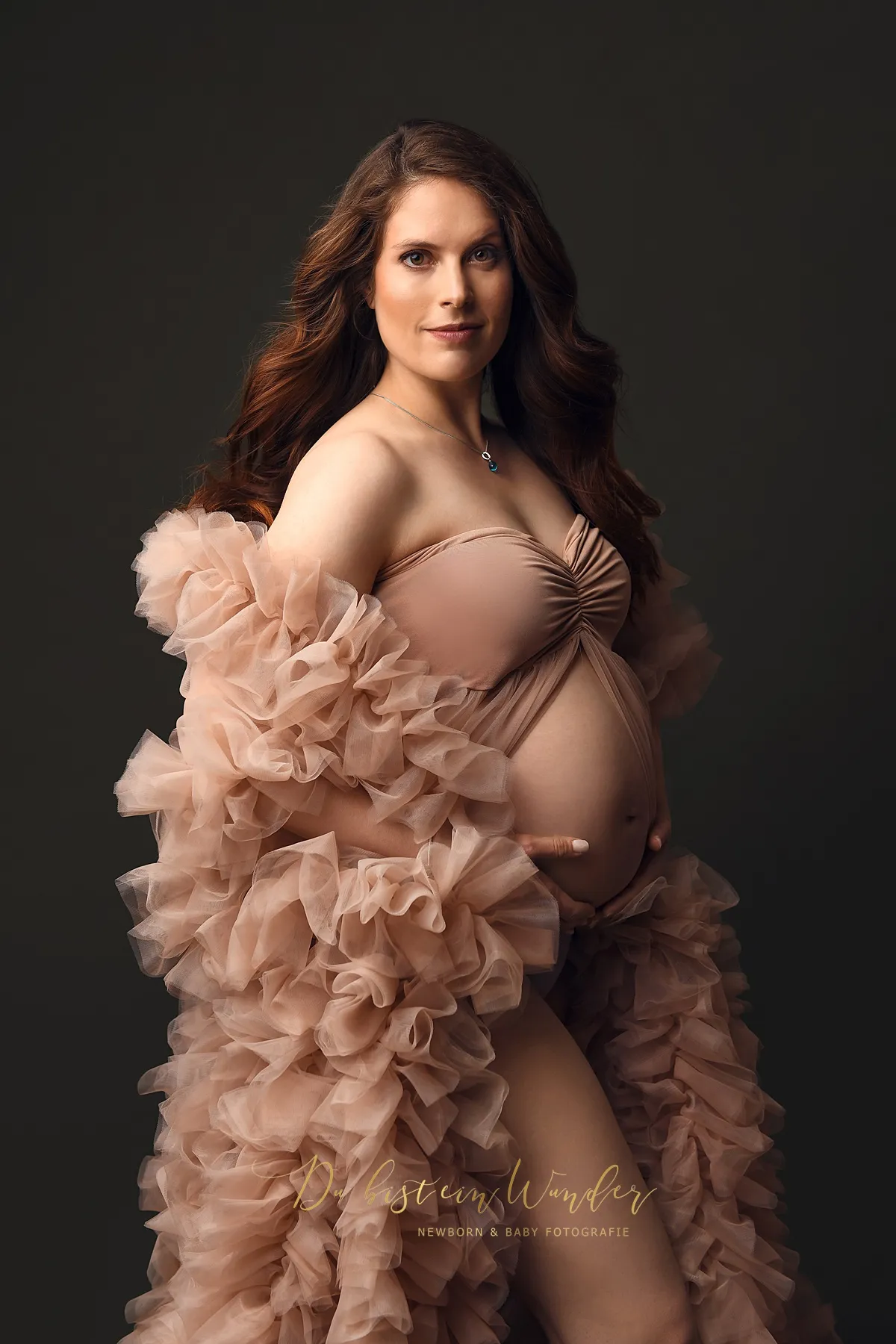 Elegantes Babybauch Portrait im beigen Rüschenkleid vor dunklem Hintergrund
