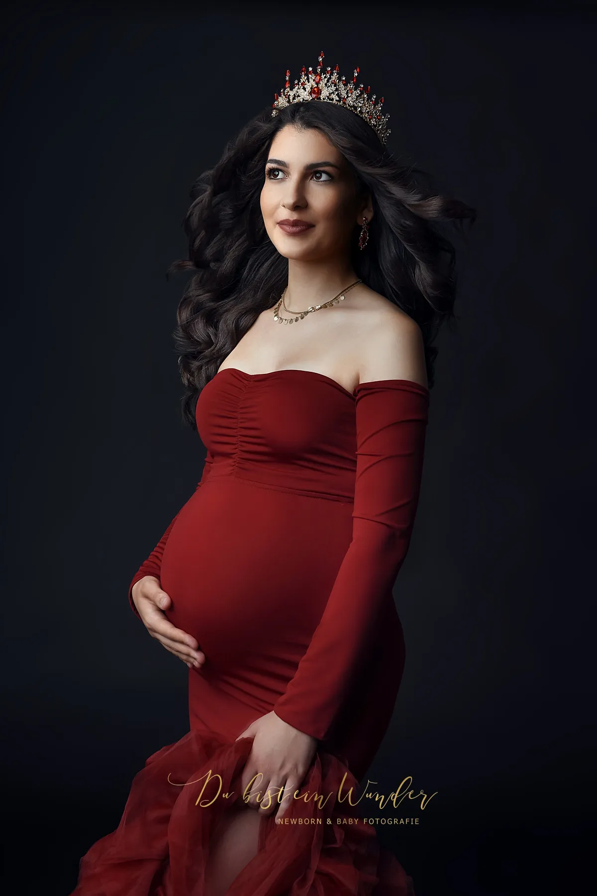 Seitliches Studio-Portrait im roten Kleid mit Krone vor dunklem Hintergrund