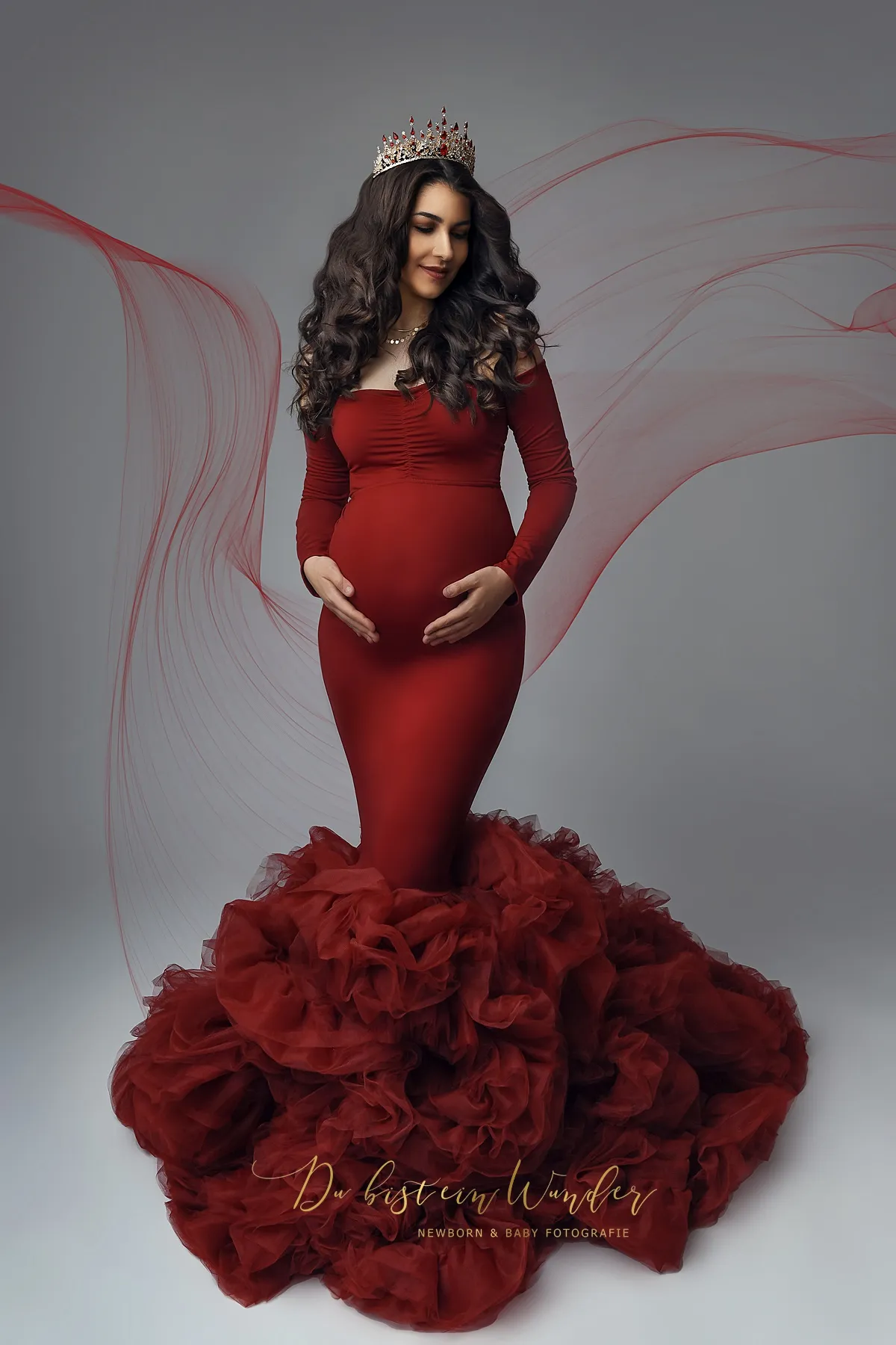 Schwangere Frau im roten Tüllkleid mit Krone und Stoffschleier im Studio