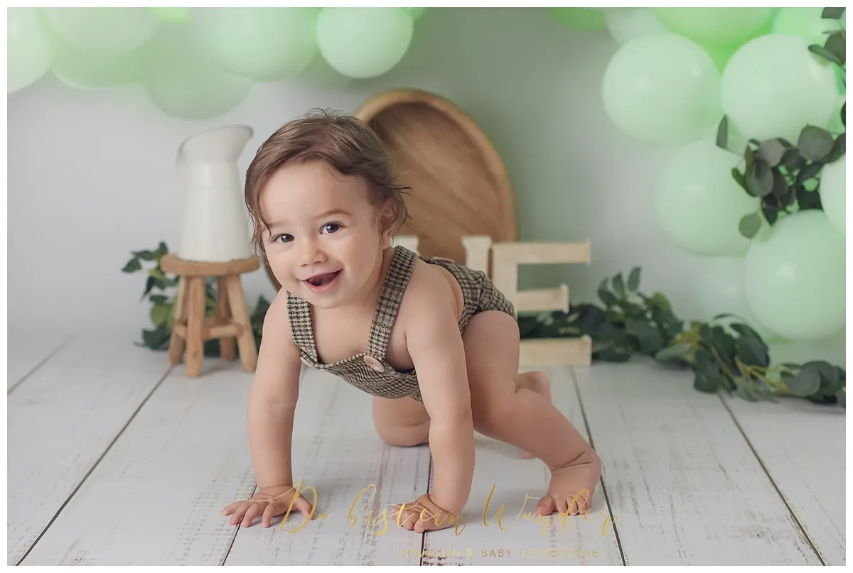 Krabbelnder Junge in Latzhose mit grünen Ballons
