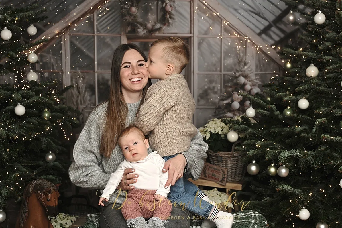 Mama mit Kleinkind und Baby im weihnachtlich geschmückten Wintergarten, der Junge gibt seiner Mama einen Kuss