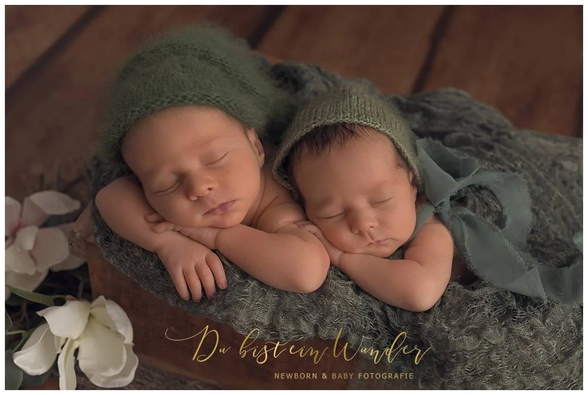 Neugeborene Zwillinge in gruenen Strickoutfits schlafend in einer Holzkiste