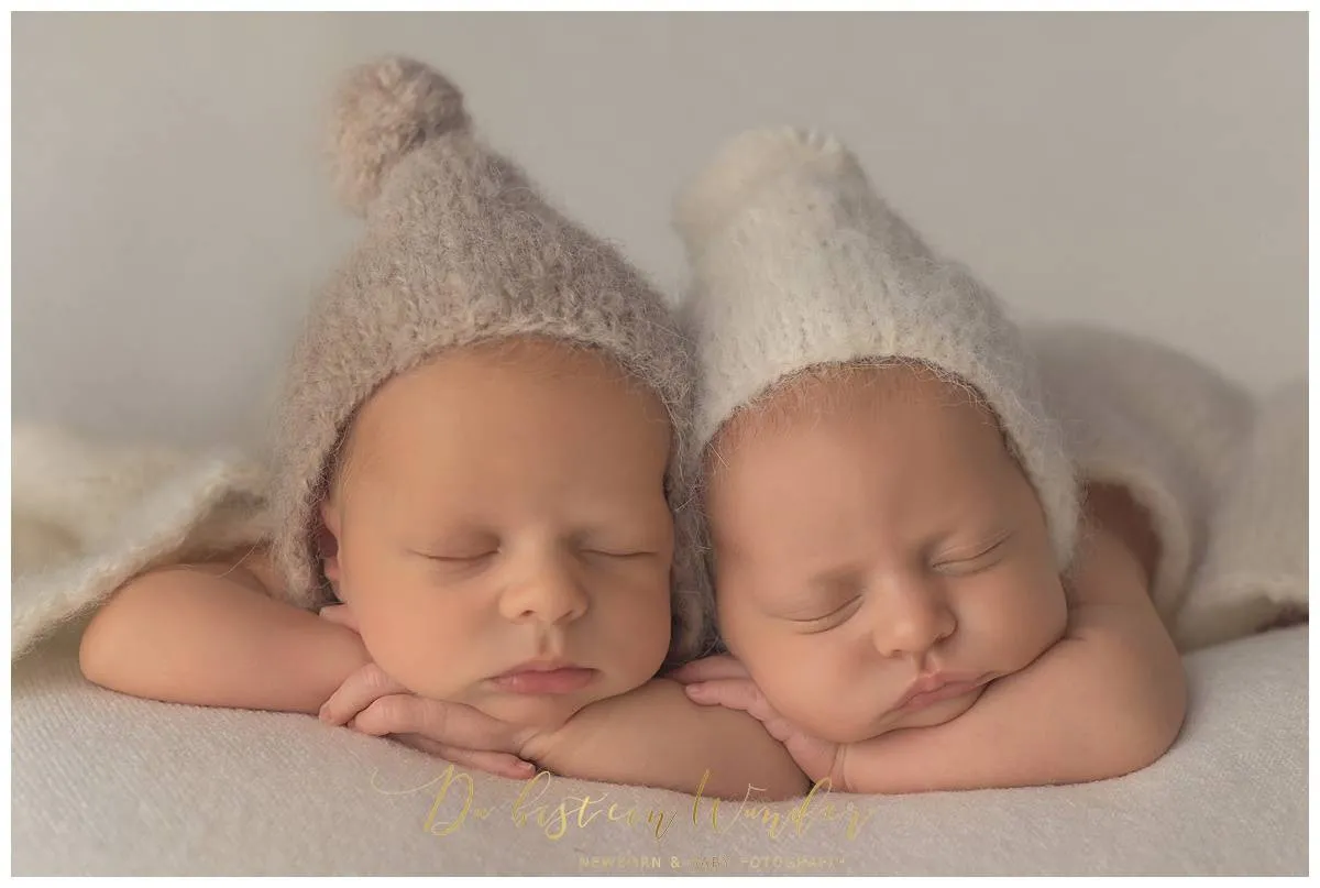 Neugeborene Zwillinge mit Strickmuetzen schlafend auf heller Decke