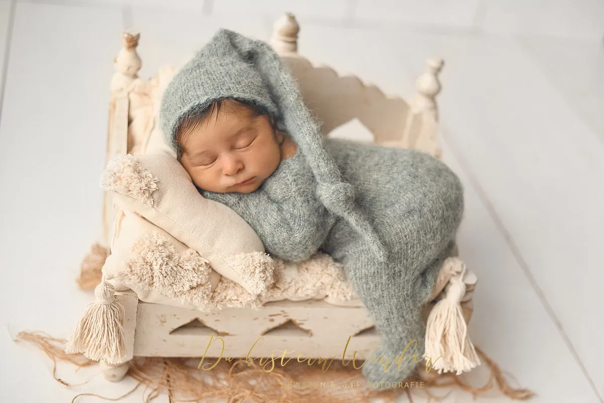 Baby mit Zipfelmütze im grauen Bett