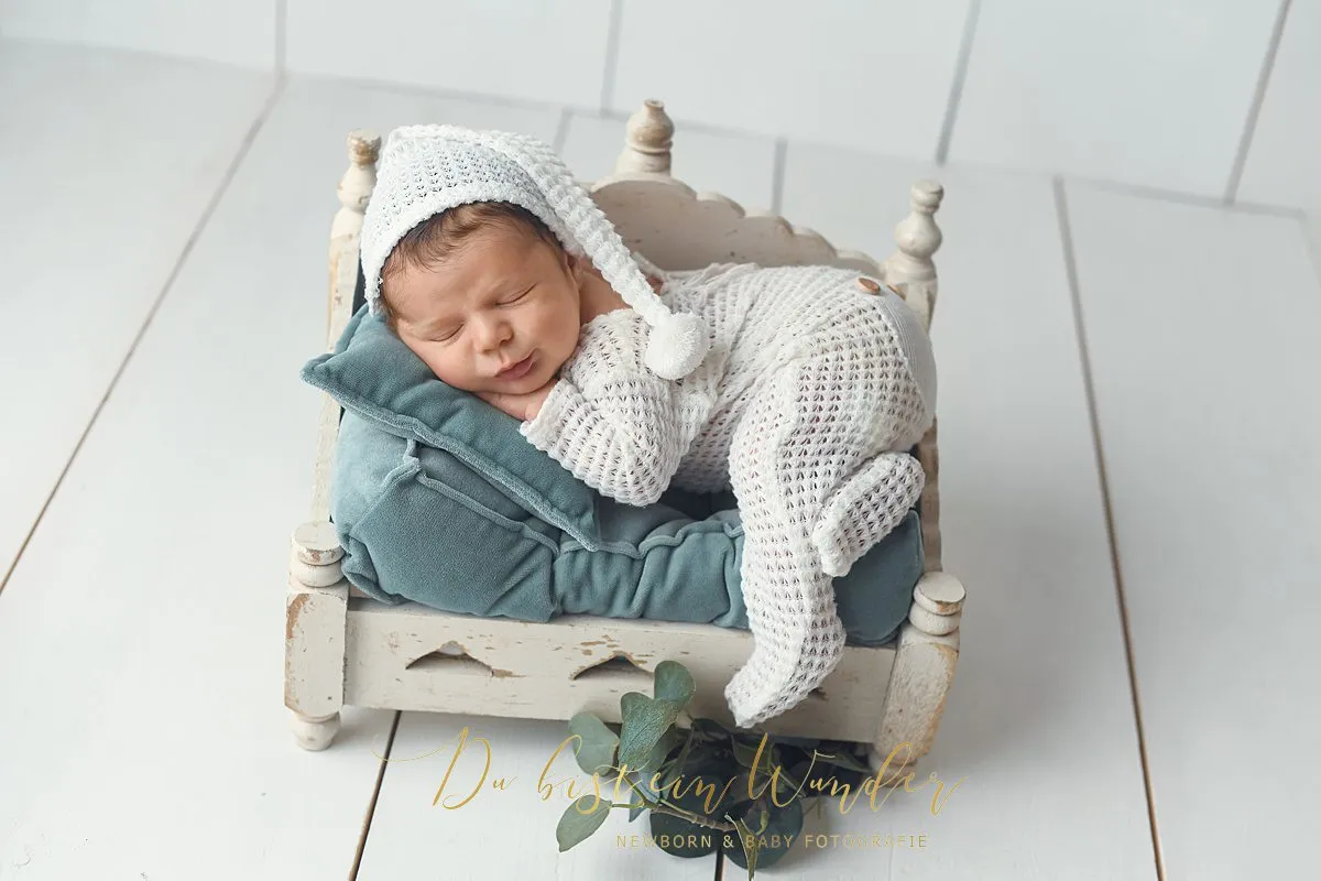 Newborn Portrait mit Mütze auf weißem Bett