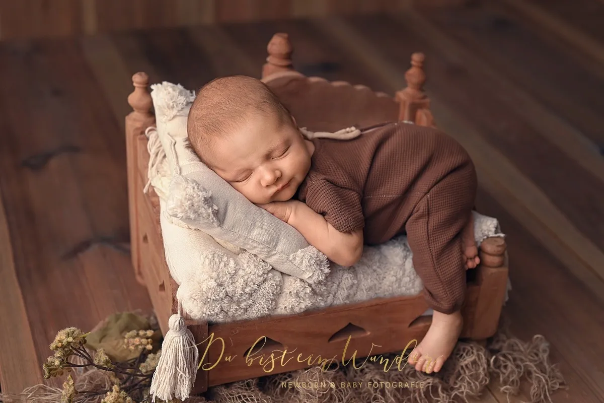 Schlafendes Neugeborenes im braunen Outfit auf einem kleinen Holzbettchen
