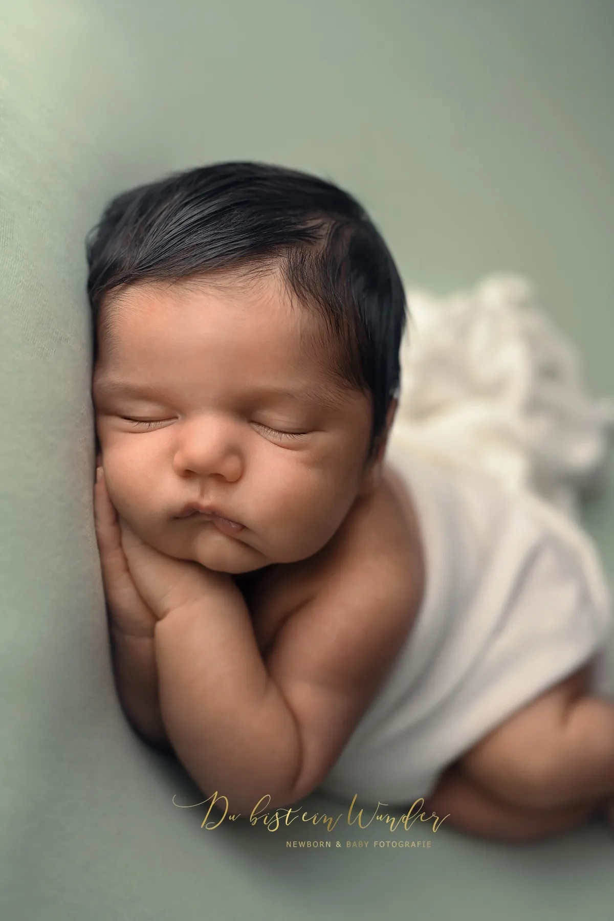 Schlafendes Neugeborenes auf mintgrünem Hintergrund in weißem Tuch eingewickelt