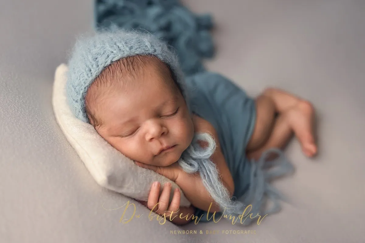 Schlafendes Neugeborenes mit blauer Strickmütze auf einem cremefarbenen Kissen