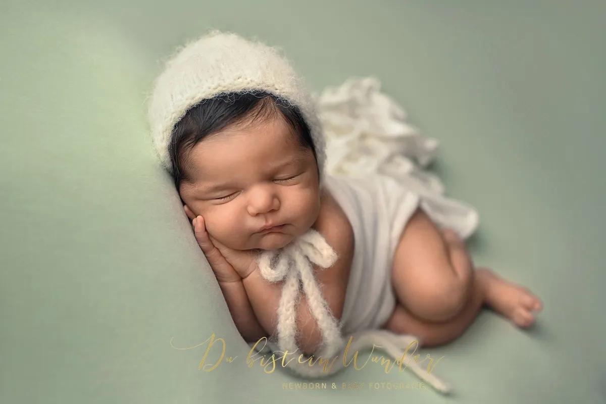 Schlafendes Neugeborenes mit weißer Strickmütze und Outfit auf mintgrünem Hintergrund