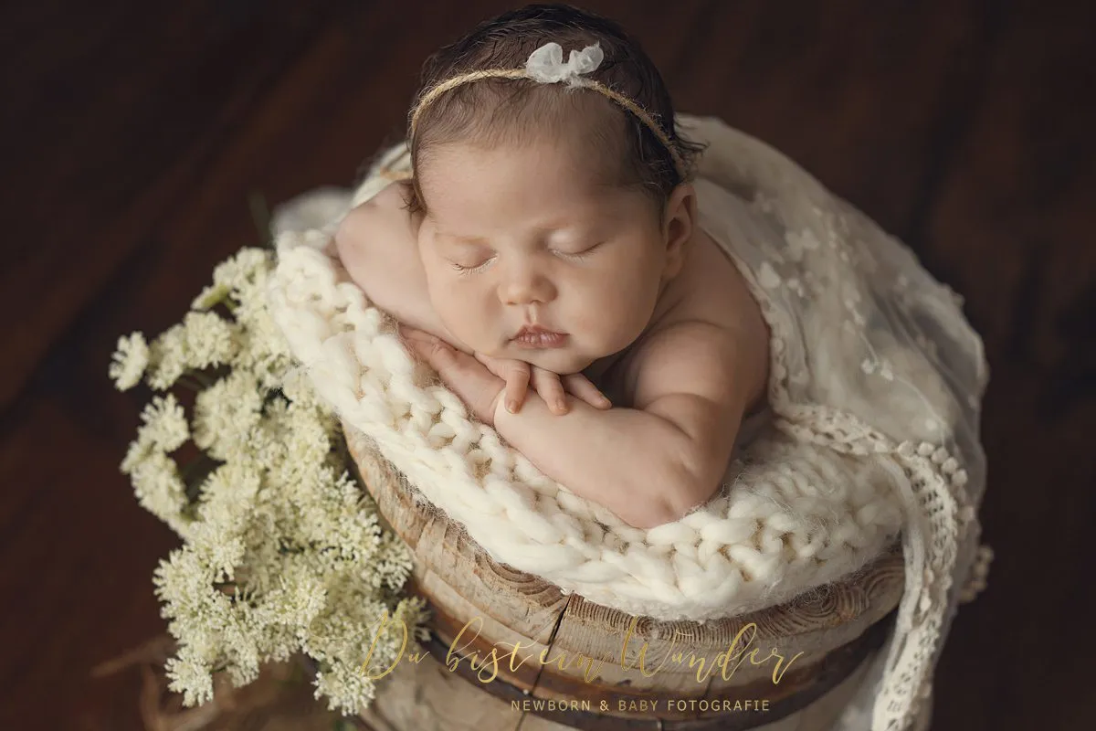 Neugeborenes im Korb mit weißer Strickdecke und Blumen