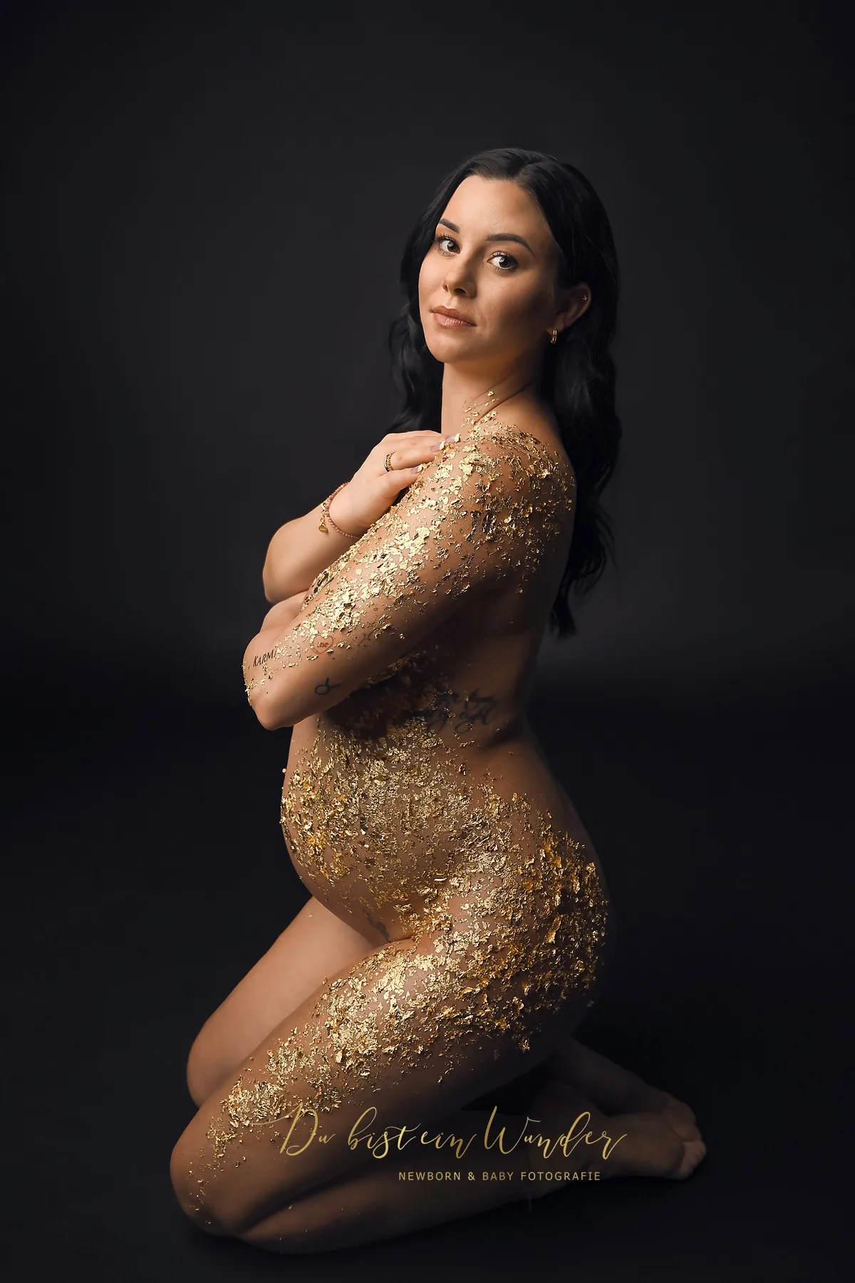 Schwangere Frau mit goldenem Blattgold vor dunklem Hintergrund