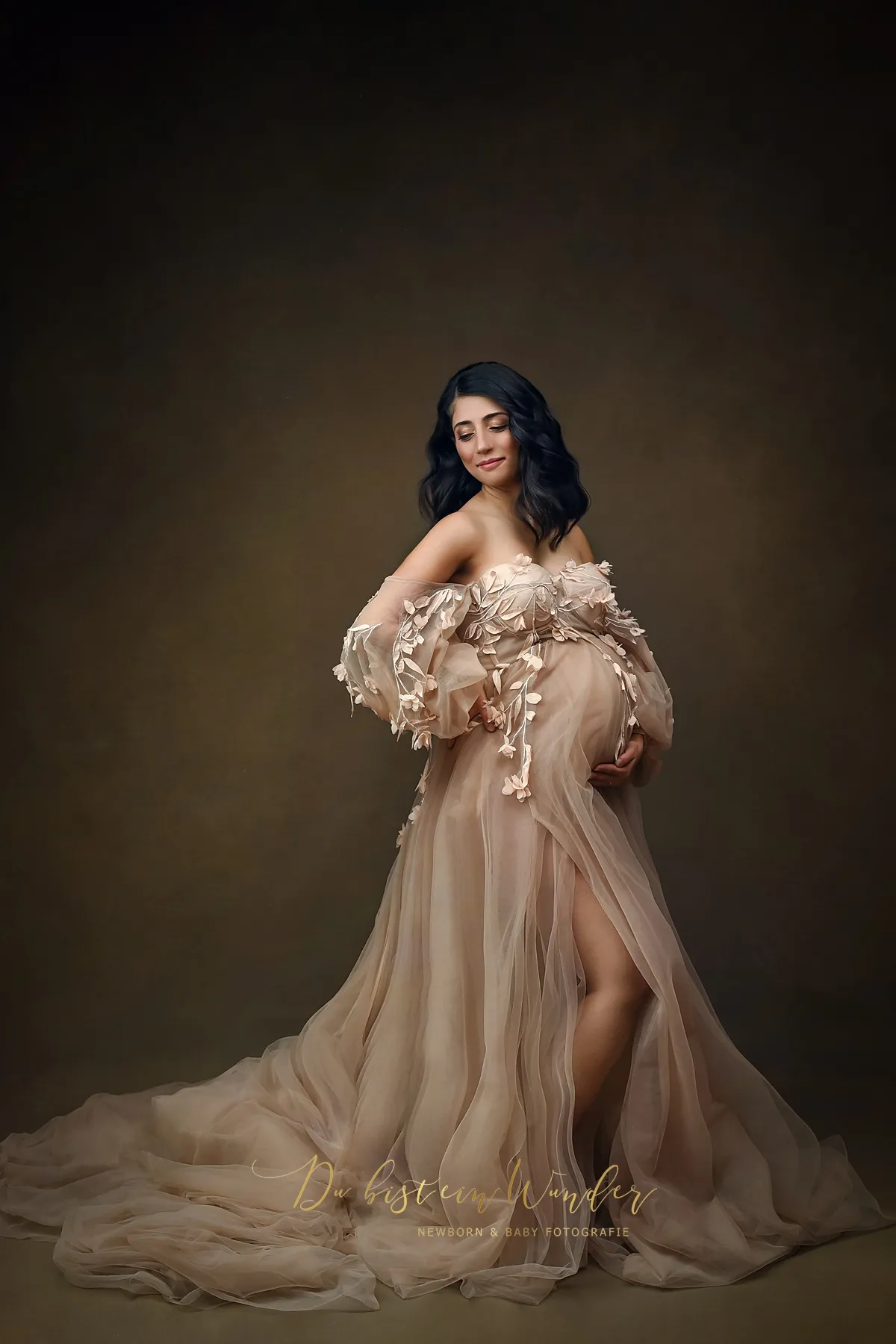 Schwangere Frau in beigem Kleid mit Blumenapplikationen bei Schwangerschaftsshooting