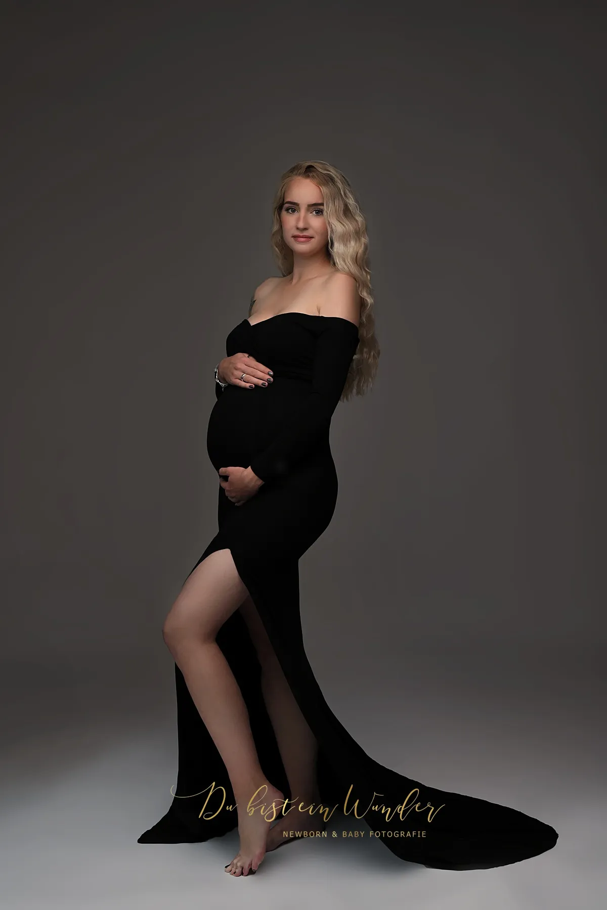 Schwangere Frau in elegantem schwarzem Kleid bei Kugelbauch-Fotoshooting