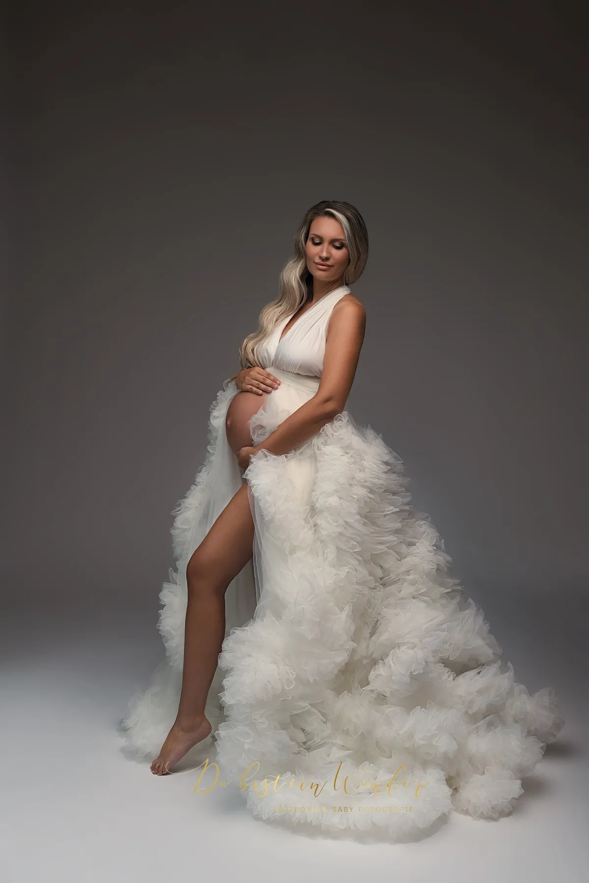 Schwangere Frau in weissem Tüllkleid bei Babybauch-Fotoshooting im Studio
