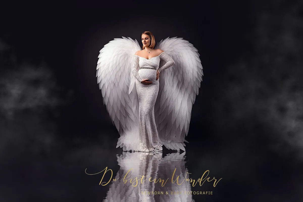 Schwangere Frau in weissem Kleid mit Engelsflügeln bei Schwangerschaftsfotografie