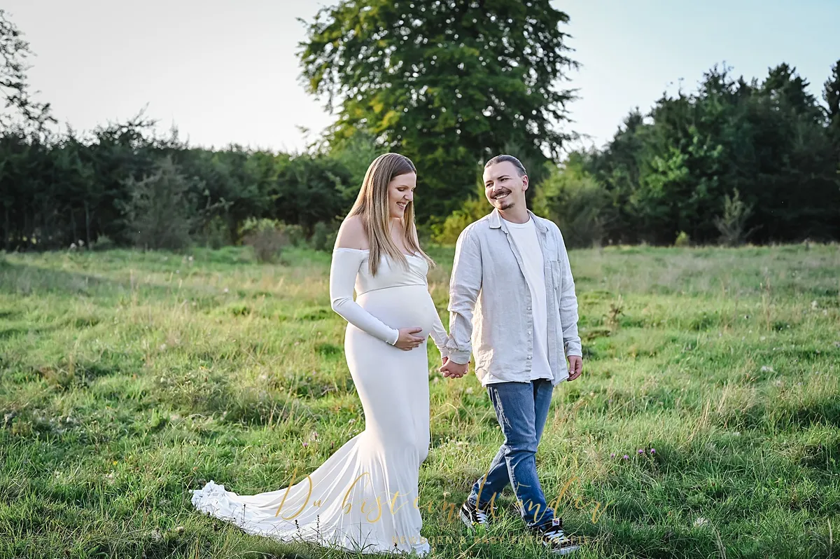 Paar auf der Wiese hält Händchen, sie im cremefarbenen Kleid