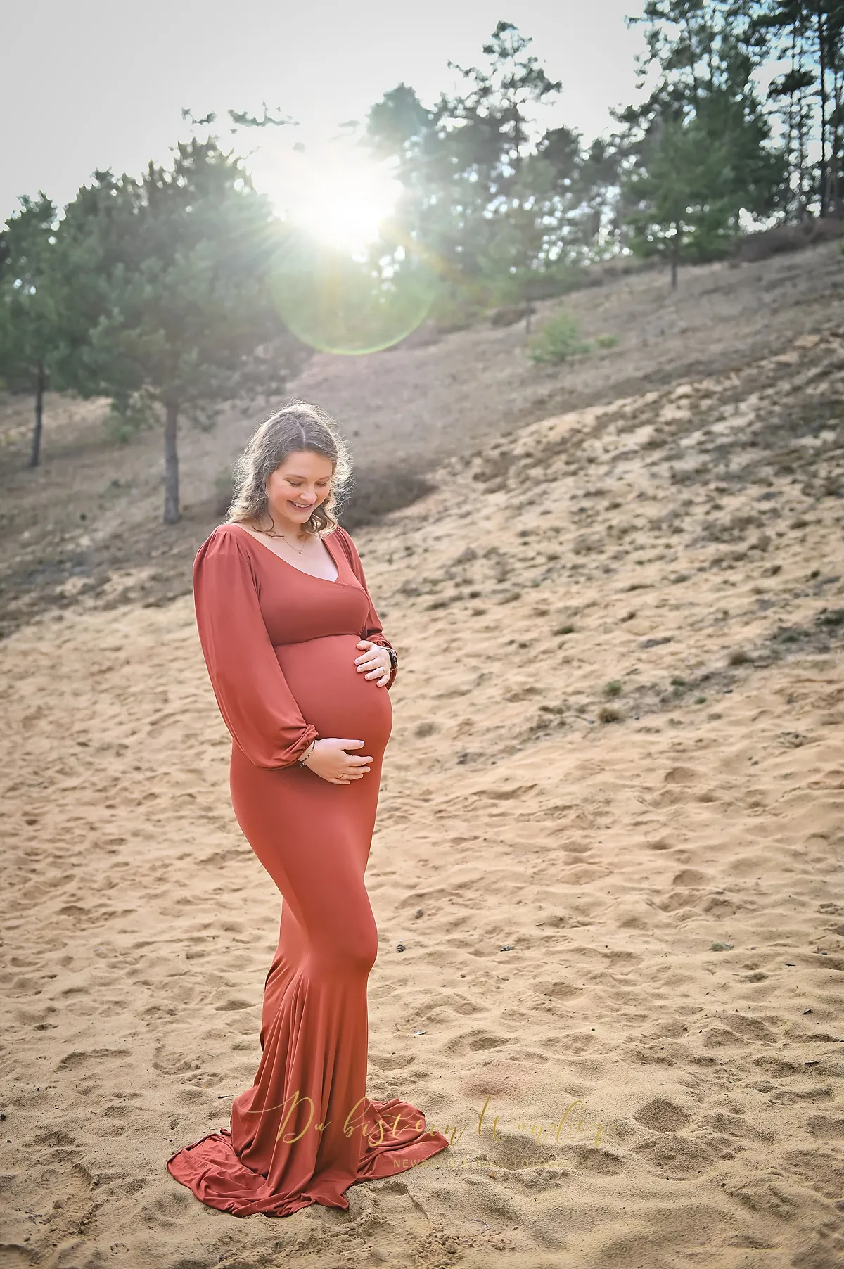 Schwangerschaftsshooting auf Sanddüne im Terracotta-Kleid bei Gegenlicht