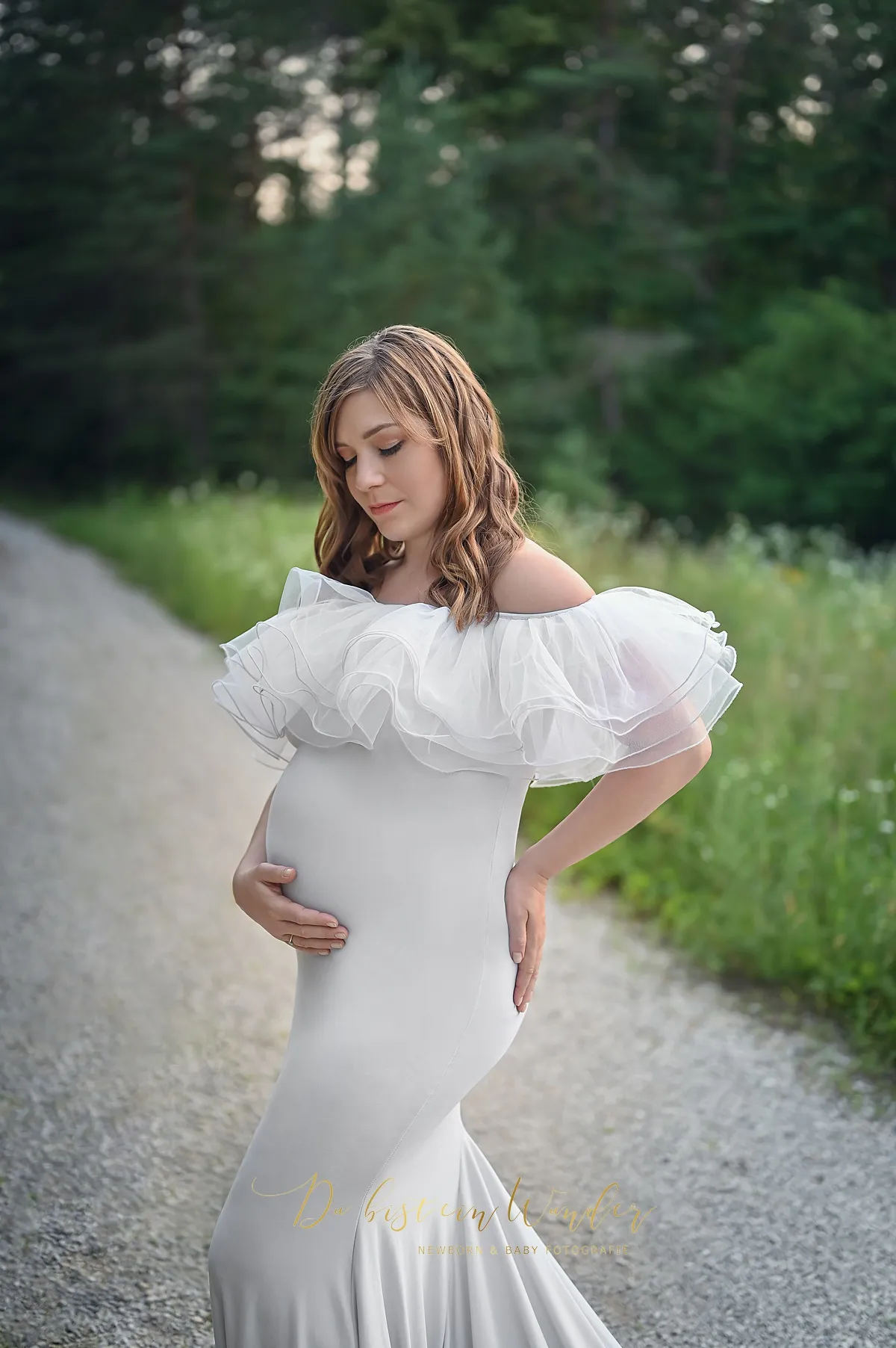Schwangere auf dem Waldweg im weißen Kleid mit Tüllrüschen
