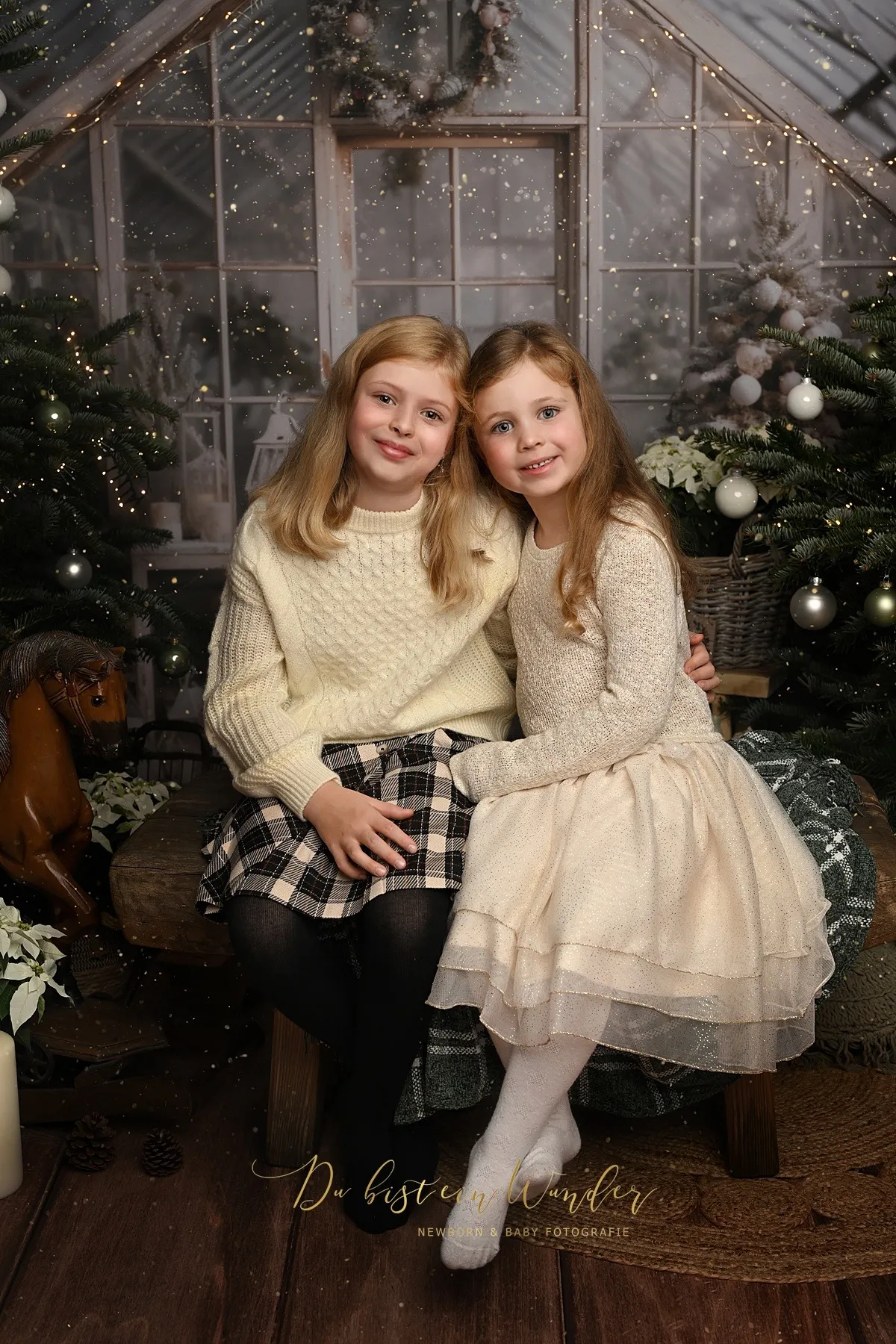 Zwei Schwestern sitzen Arm in Arm im weihnachtlich geschmückten Wintergarten mit Lichterketten